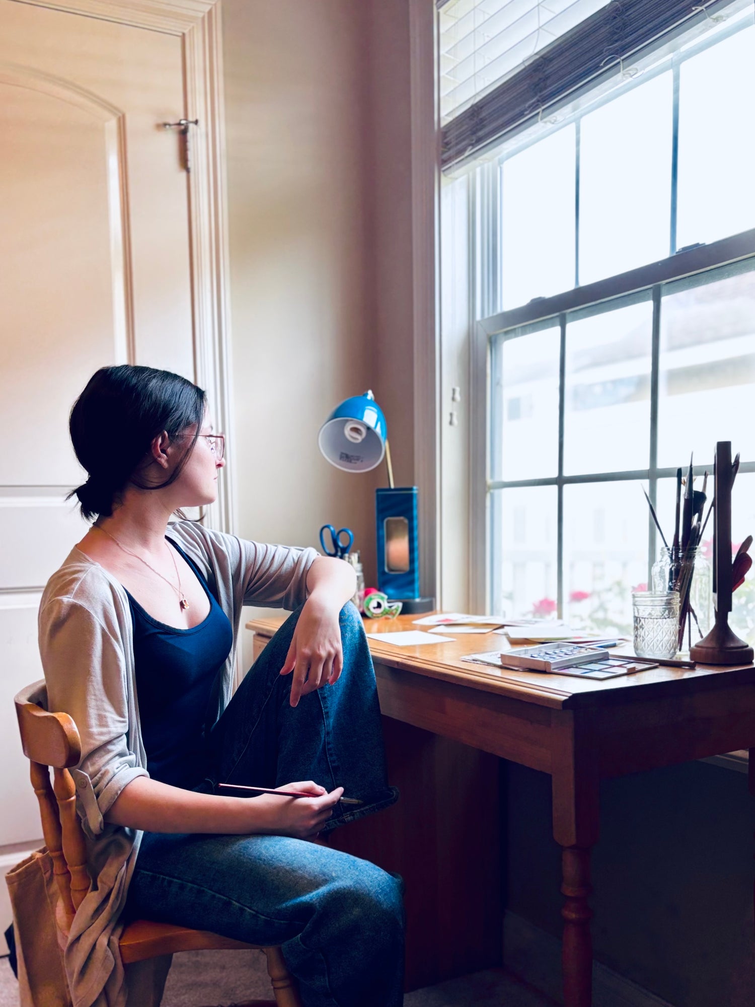 Store owner sitting at her paint desk by a window in a home office setting. 