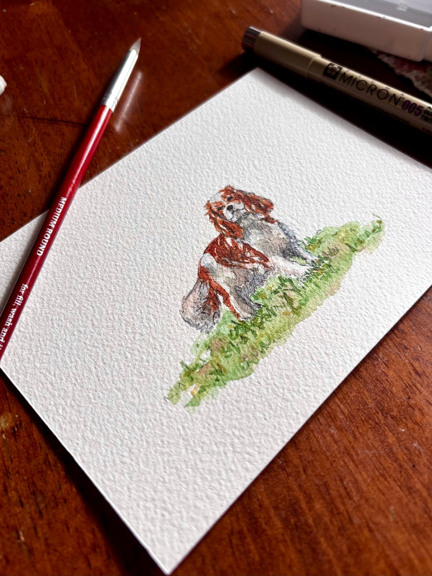 Watercolor painting of a spaniel on a piece of paper with a paintbrush and pencil on a wooden surface.