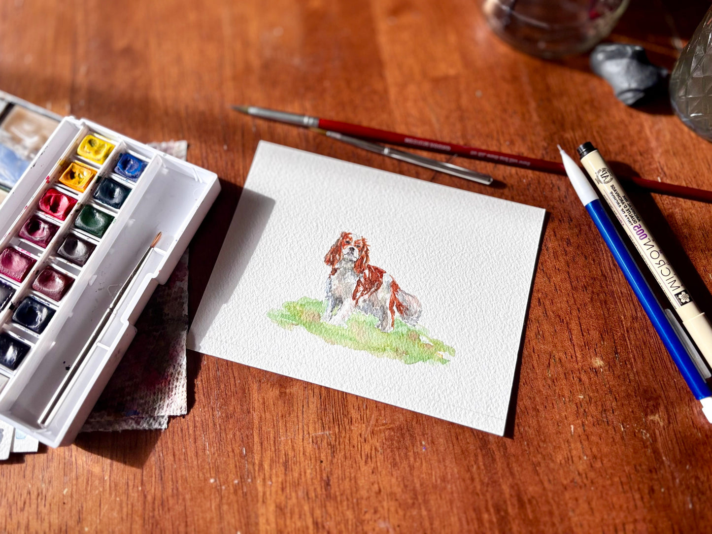 Watercolor painting of a dog on paper with art supplies on a wooden surface.