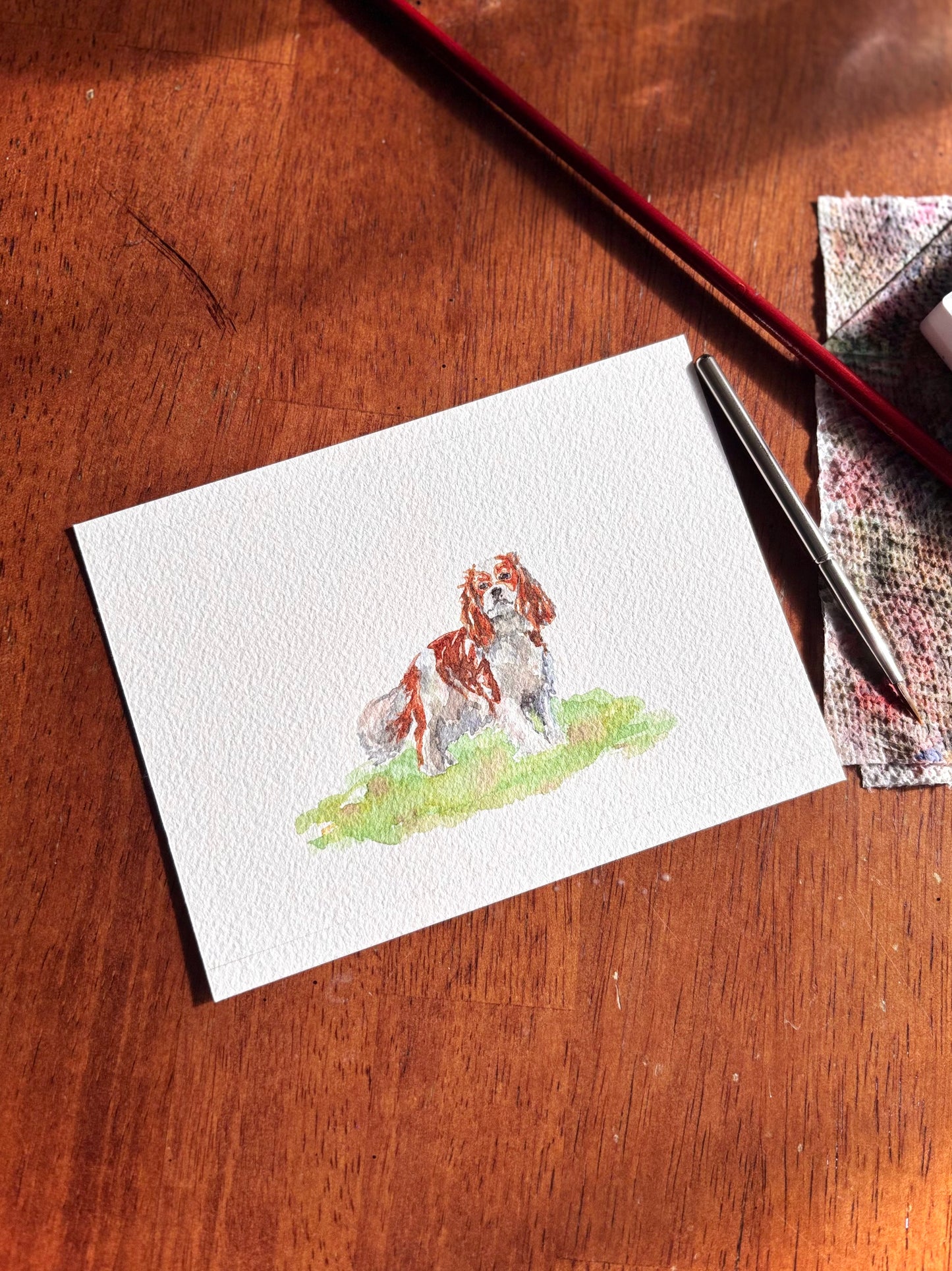 Miniature painting with a spaniel dog illustration on a wooden surface with a pen and paper.