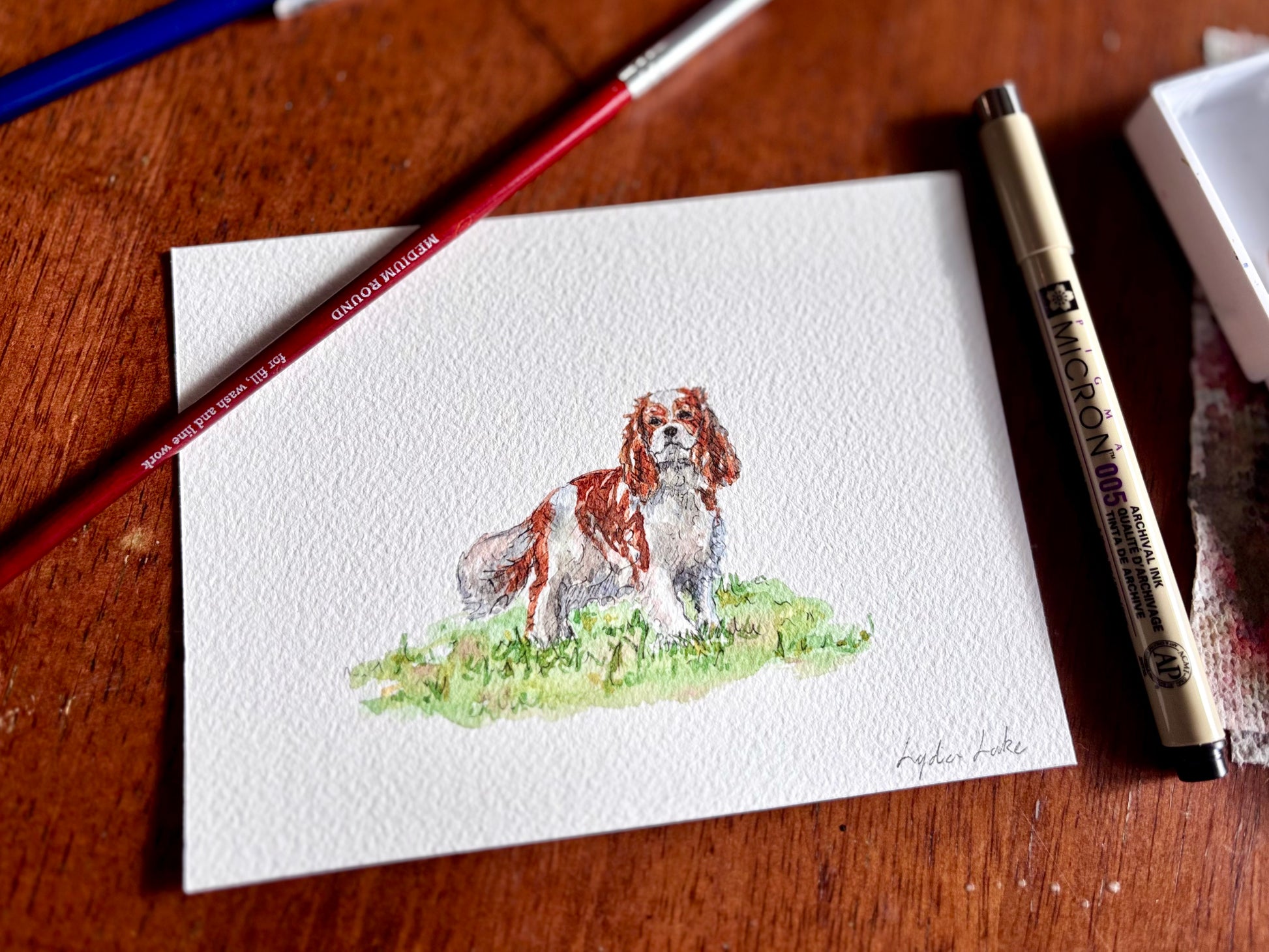 Watercolor painting of a dog on a piece of paper with professional art supplies on a wooden surface.