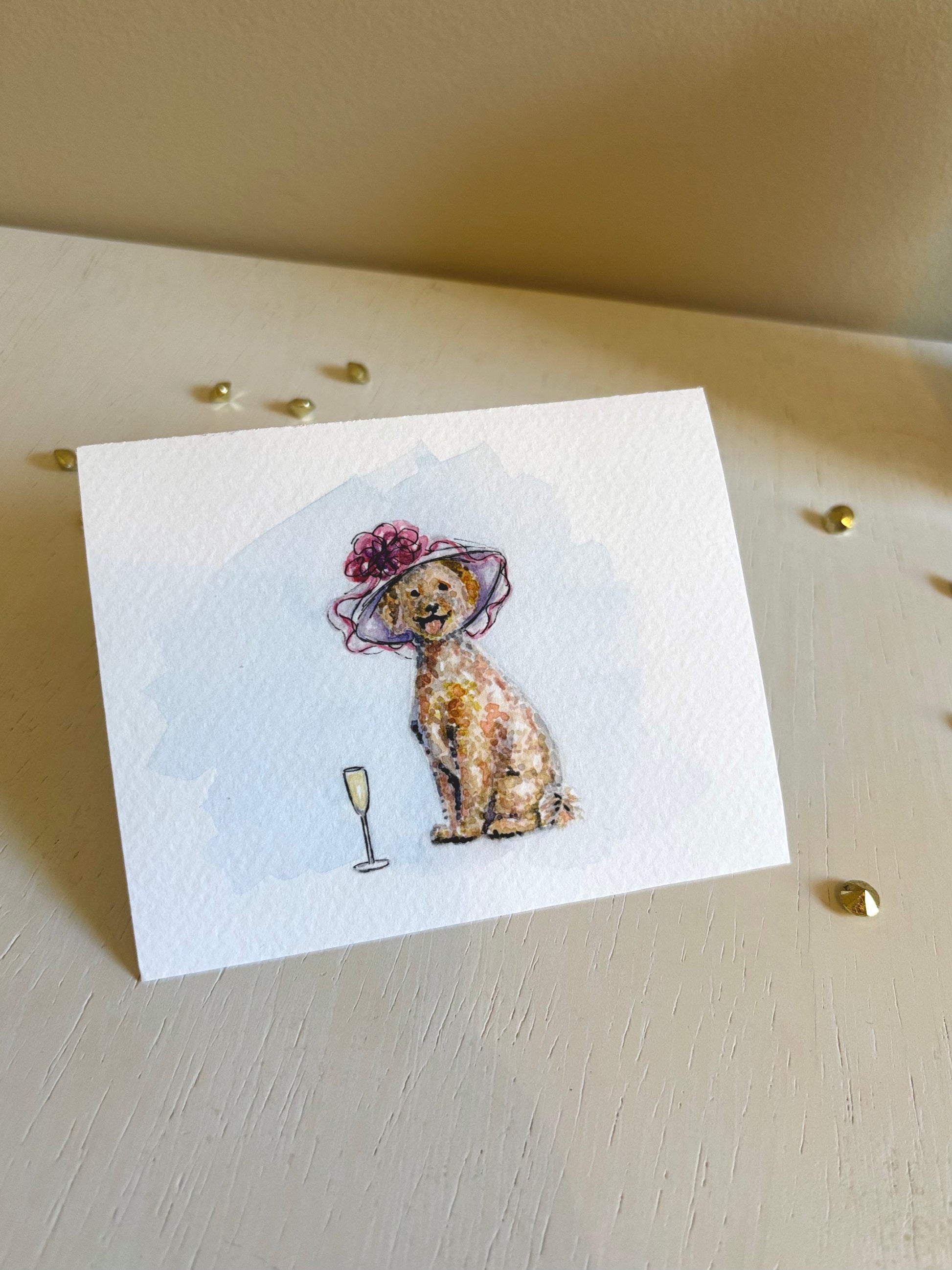 Miniature fine art print with a Golden Doodle illustration wearing a hat and holding a glass on a beige surface.