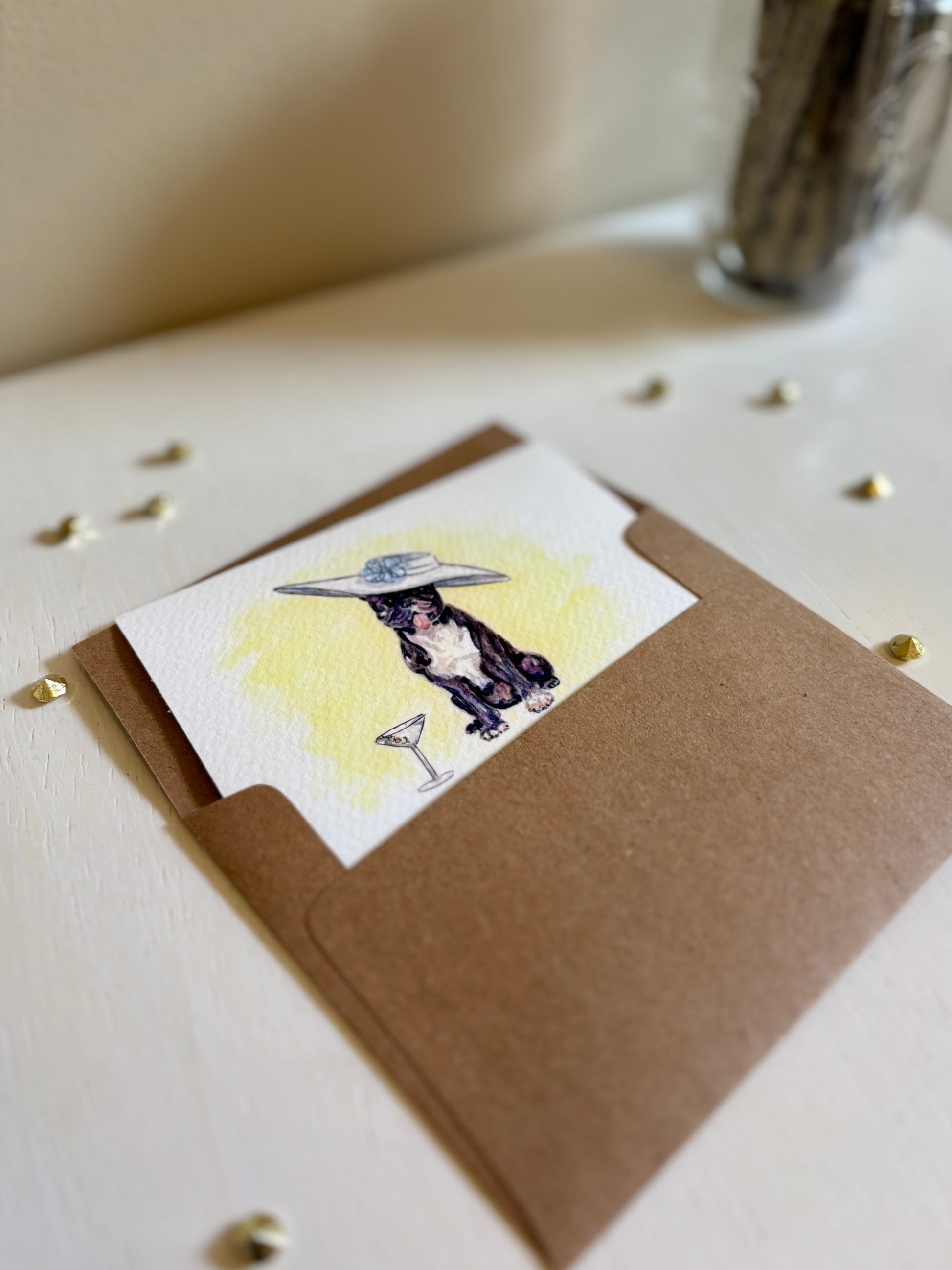 Miniature watercolor art print with a dog illustration in a brown envelope on a light surface.