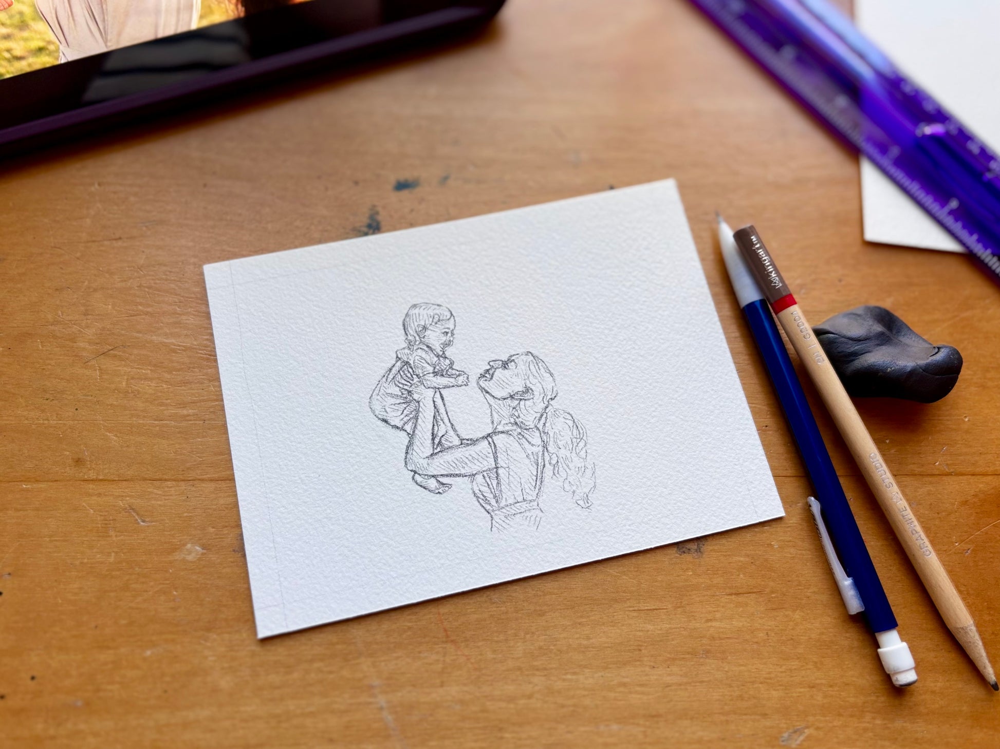 Artistic drawing of a mother and child on a piece of paper with art supplies on a wooden surface.